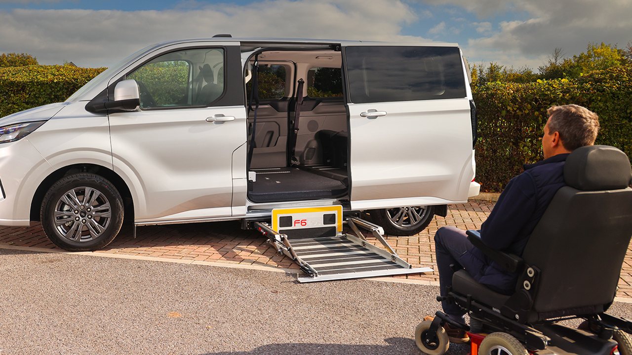 Wheelchair user about to board a white Ford Custom Colorado by its side ramp.