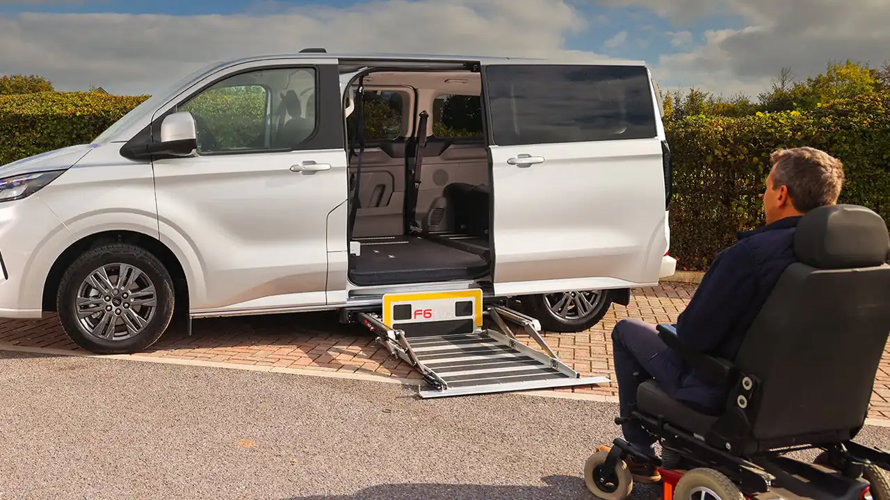 Wheelchair user about to board a white Ford Custom Colorado by its side ramp.