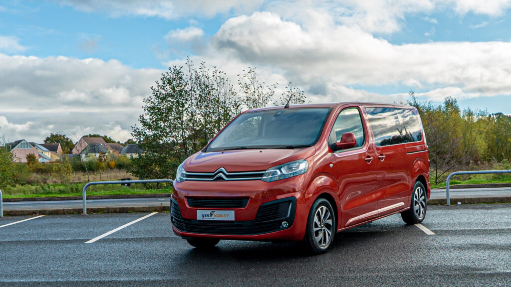 Red Citroën van parked on asphalt near countryside, under a cloudy sky.