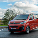 Red Citroën van parked on asphalt near countryside, under a cloudy sky.